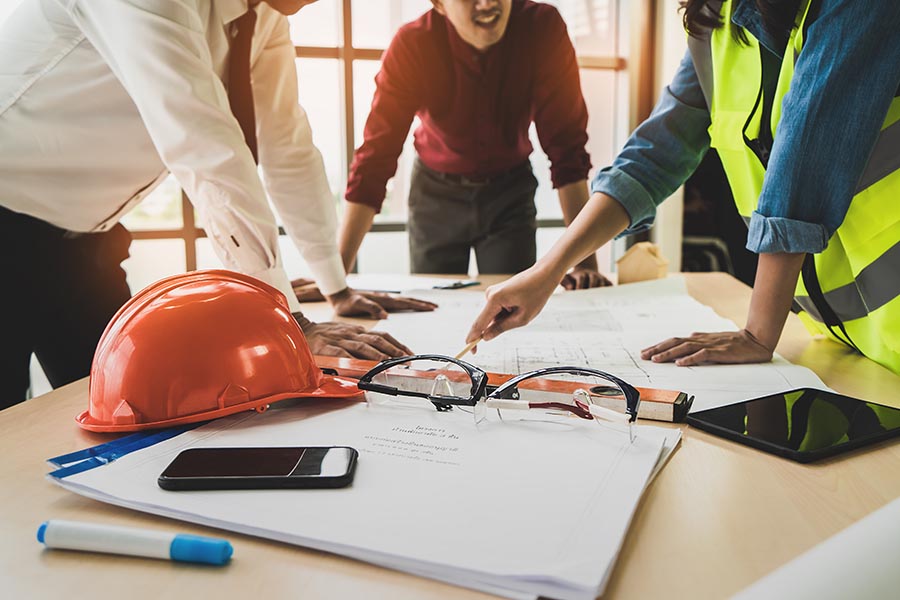 Specialized Business Insurance - Contractor and Architects Discuss Plans for New Construction, Hard Hats and Schematic Drawings on the Table